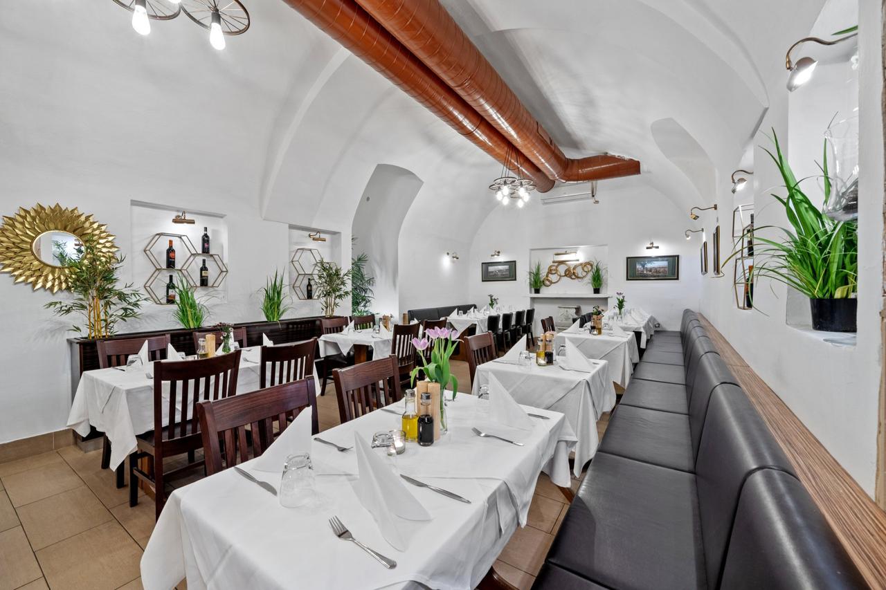 Gewölbekeller des Restaurant Volare in Wien mit weiß eingedeckten Tischen, Lederbank und Hexagon-Weinregal