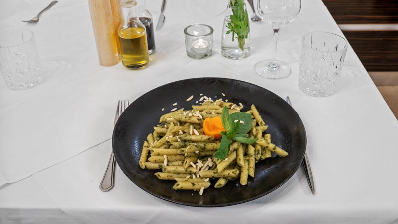 Hausgemachte Penne mit Pesto, Pinienkernen und Basilikum auf schwarzem Teller